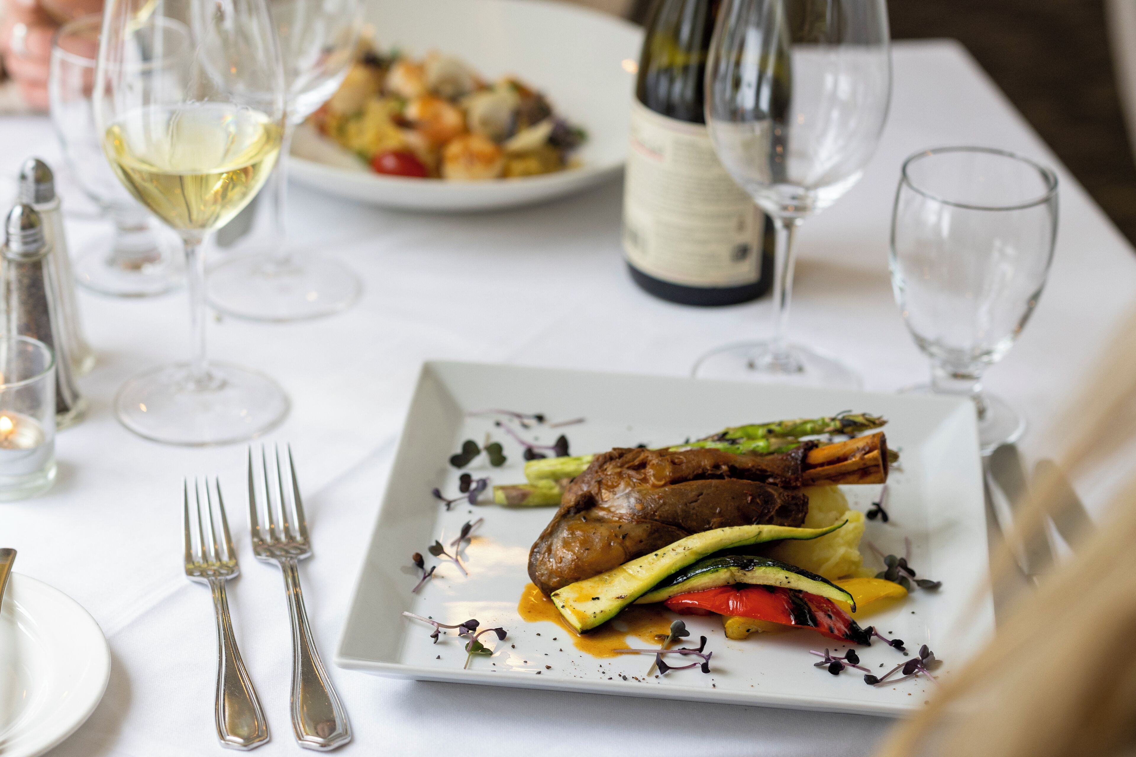 A dining table with plates of food, wine glasses, and cutlery.