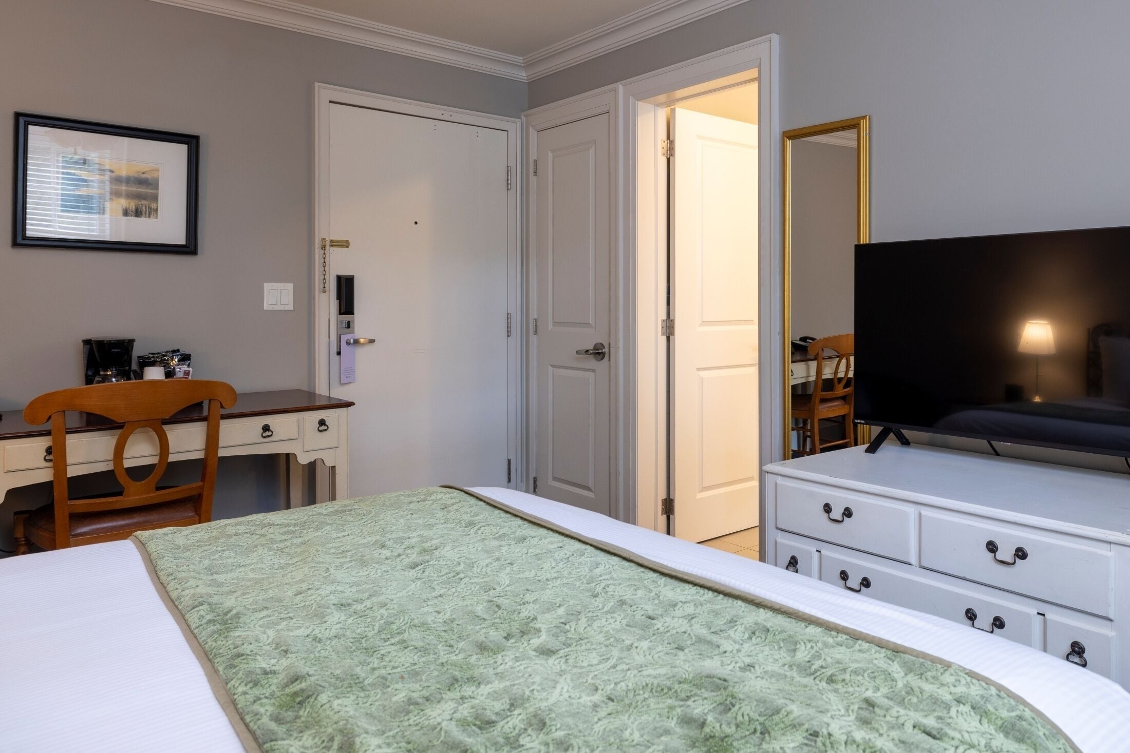 Quarto de hotel com uma cama, escrivaninha com cadeira, televisão e cômoda.