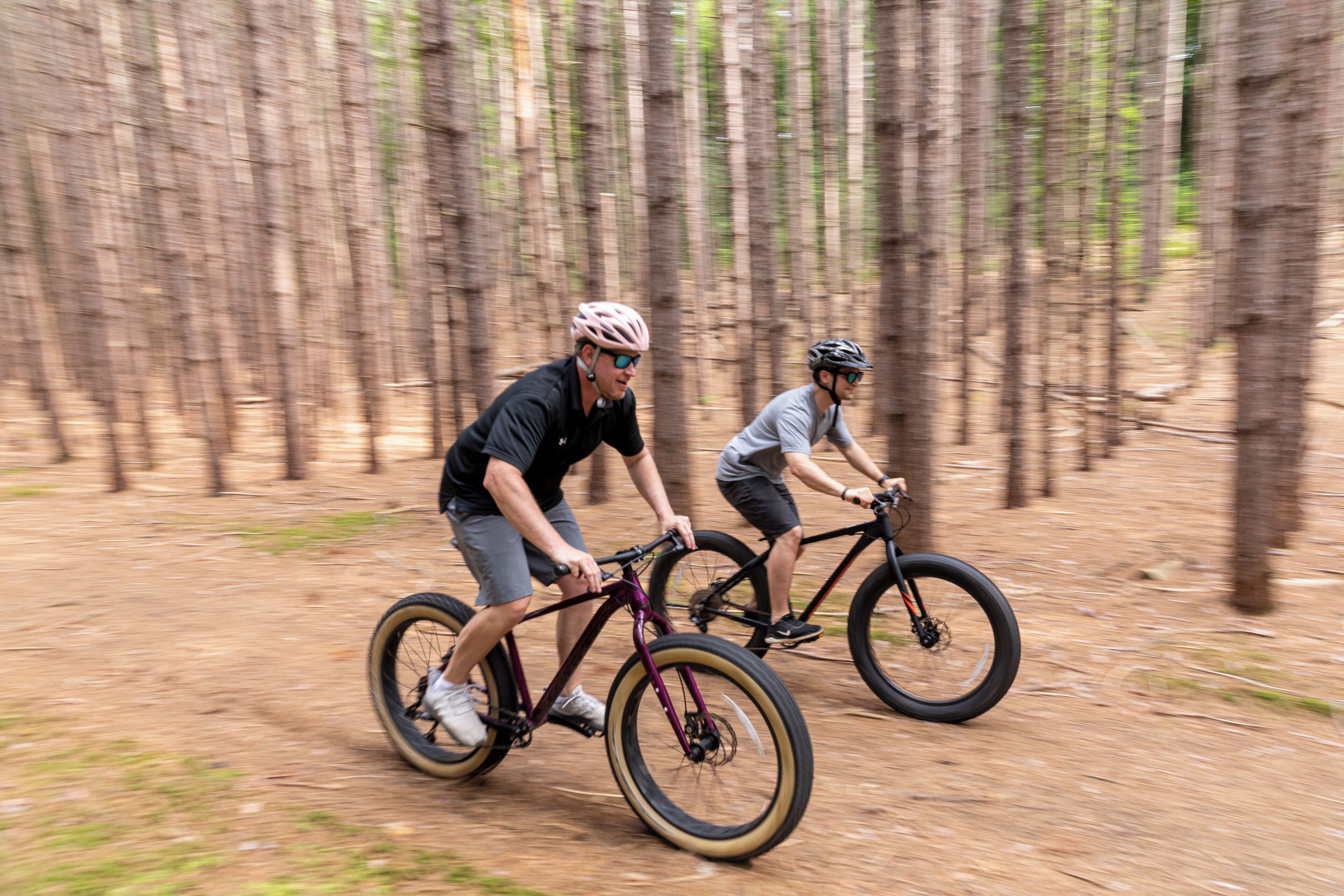 Dos personas pedaleando en bicicleta por un sendero de tierra rodeado de árboles.