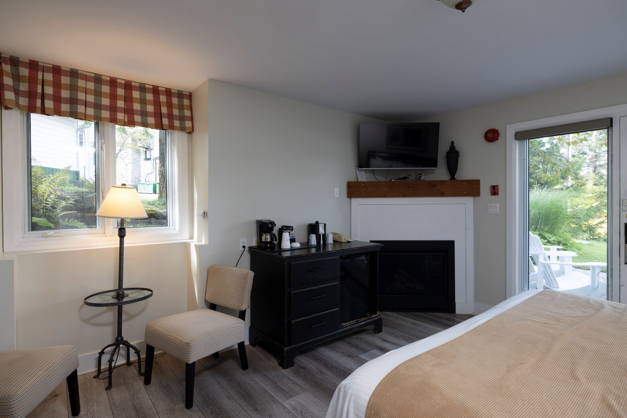 Habitación de hotel con cama, escritorio con lámpara, silla, televisor en un estante y vistas al exterior.