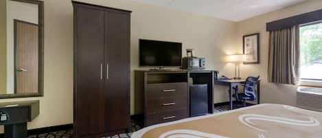 A hotel room with a large bed, a desk with a computer, a television, a wardrobe, and a mirror.