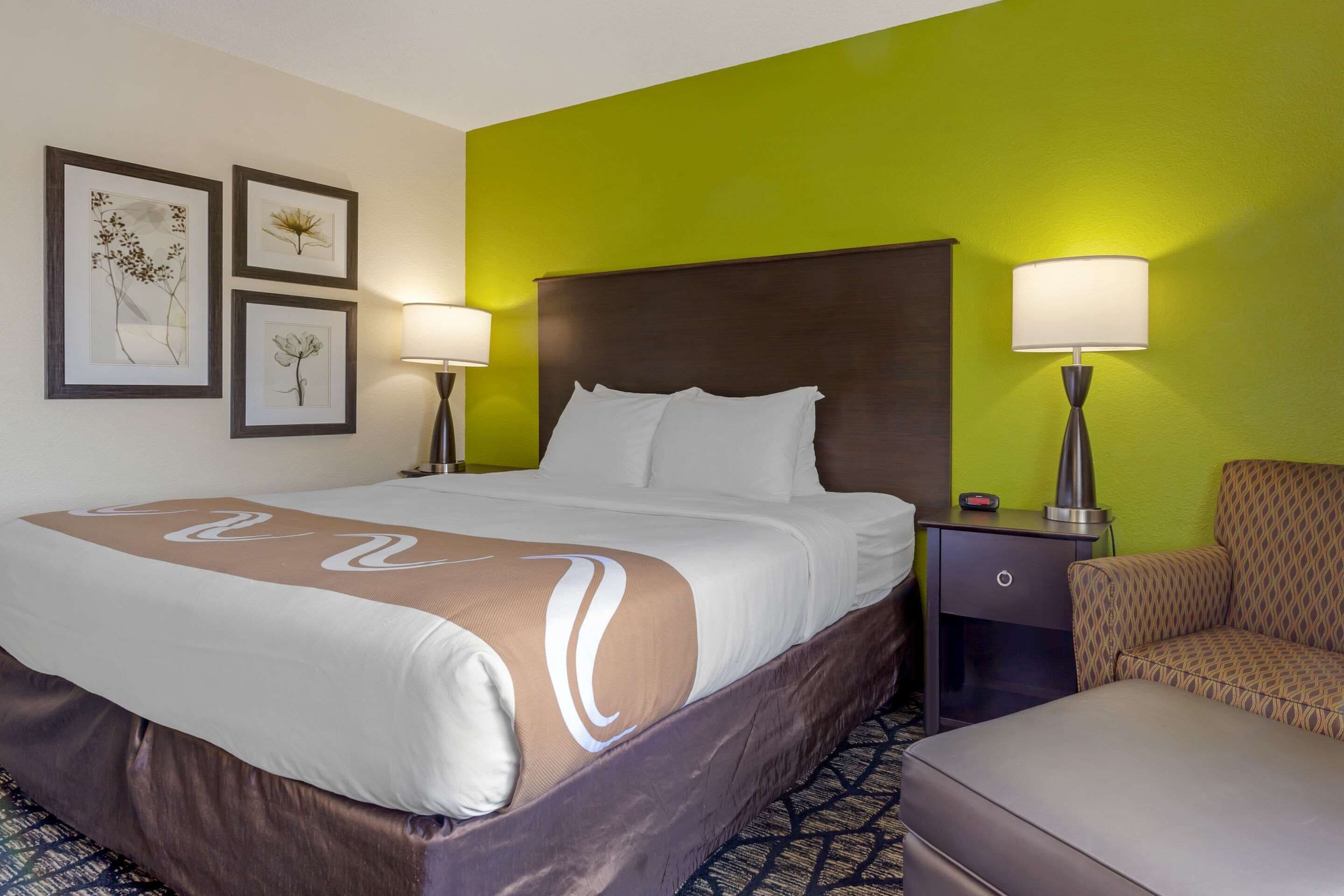 A hotel room with a large bed, two bedside tables, a chair, and artwork on the wall.