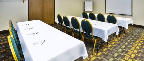 A conference room with a long table, chairs, a whiteboard, and a projector screen.