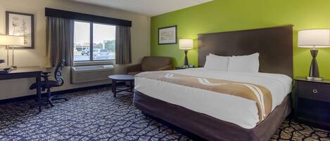 A hotel room with a large bed, a desk, a chair, and a window with curtains.