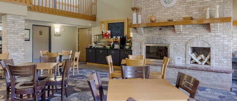 A dining area with wooden tables and chairs, a brick fireplace, and a mezzanine level with a wooden railing.