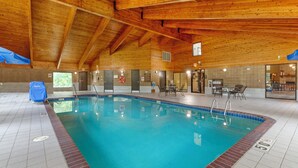 Una piscina interior con vigas de madera, suelo de baldosas y una silla de salvavidas.
