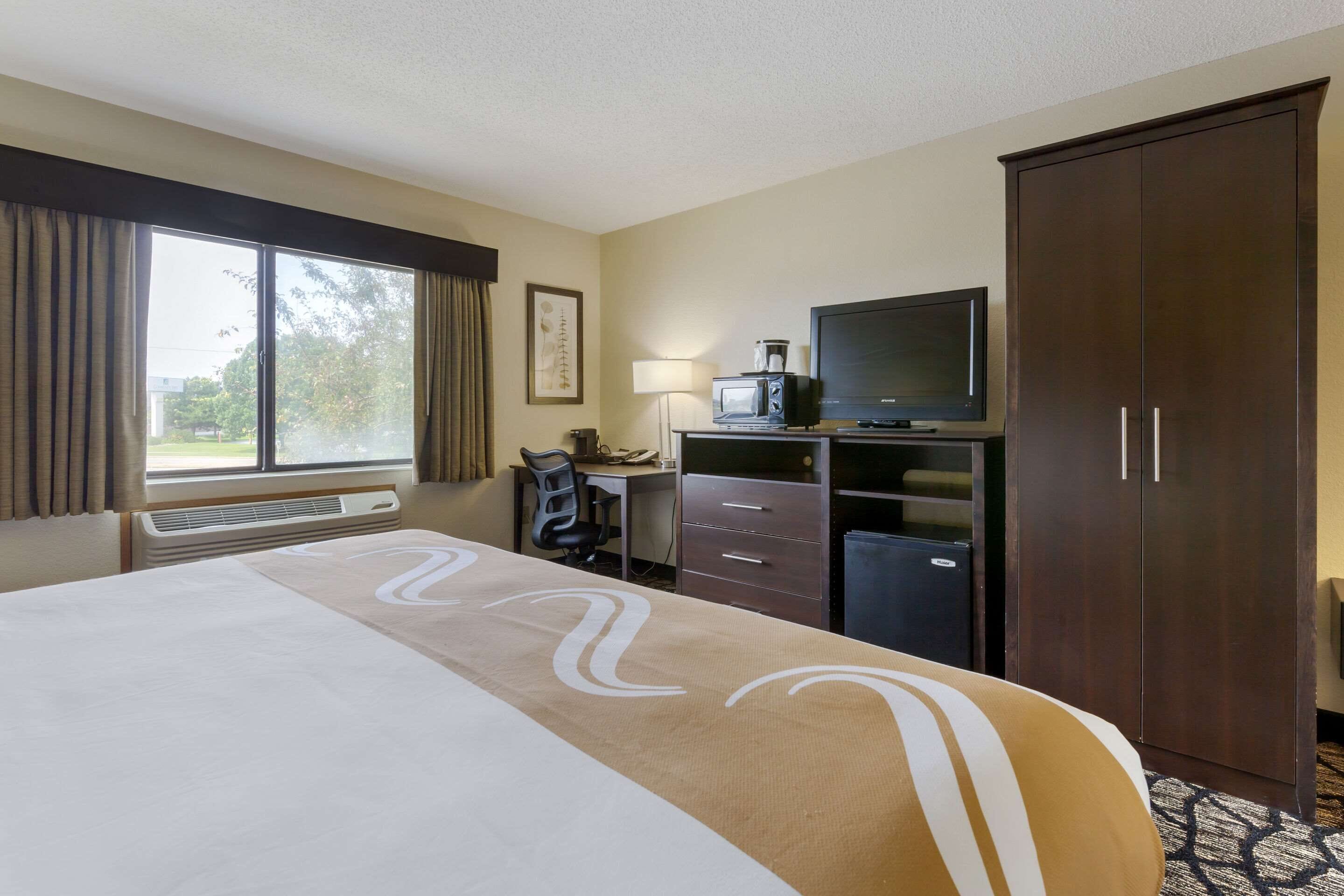 A hotel room with a large bed, a desk with a computer, a television, and a wardrobe.