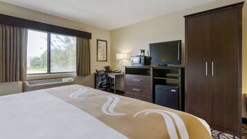 A hotel room with a large bed, a desk with a computer, a television, and a wardrobe.