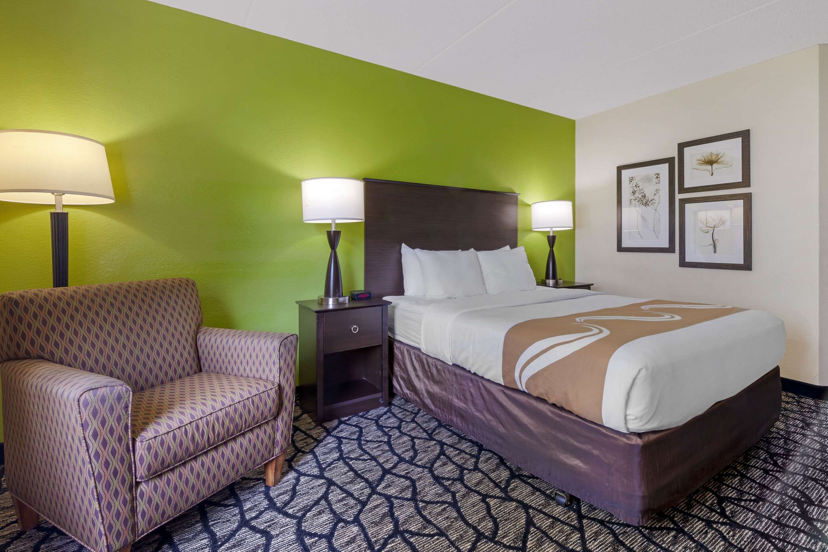 A hotel room with a bed, two bedside lamps, a chair, and a nightstand.