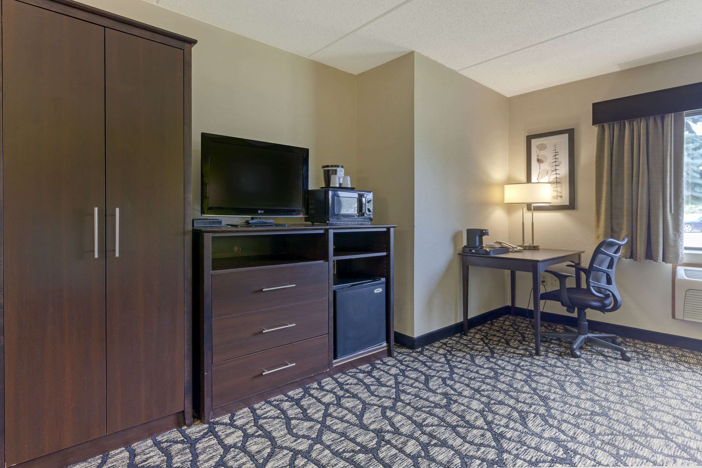 A hotel room with a large wardrobe, a desk with a chair, a television, a microwave, and a small refrigerator.