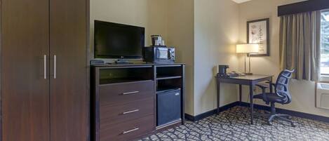 A hotel room with a large wardrobe, a desk with a chair, a television, a microwave, and a small refrigerator.