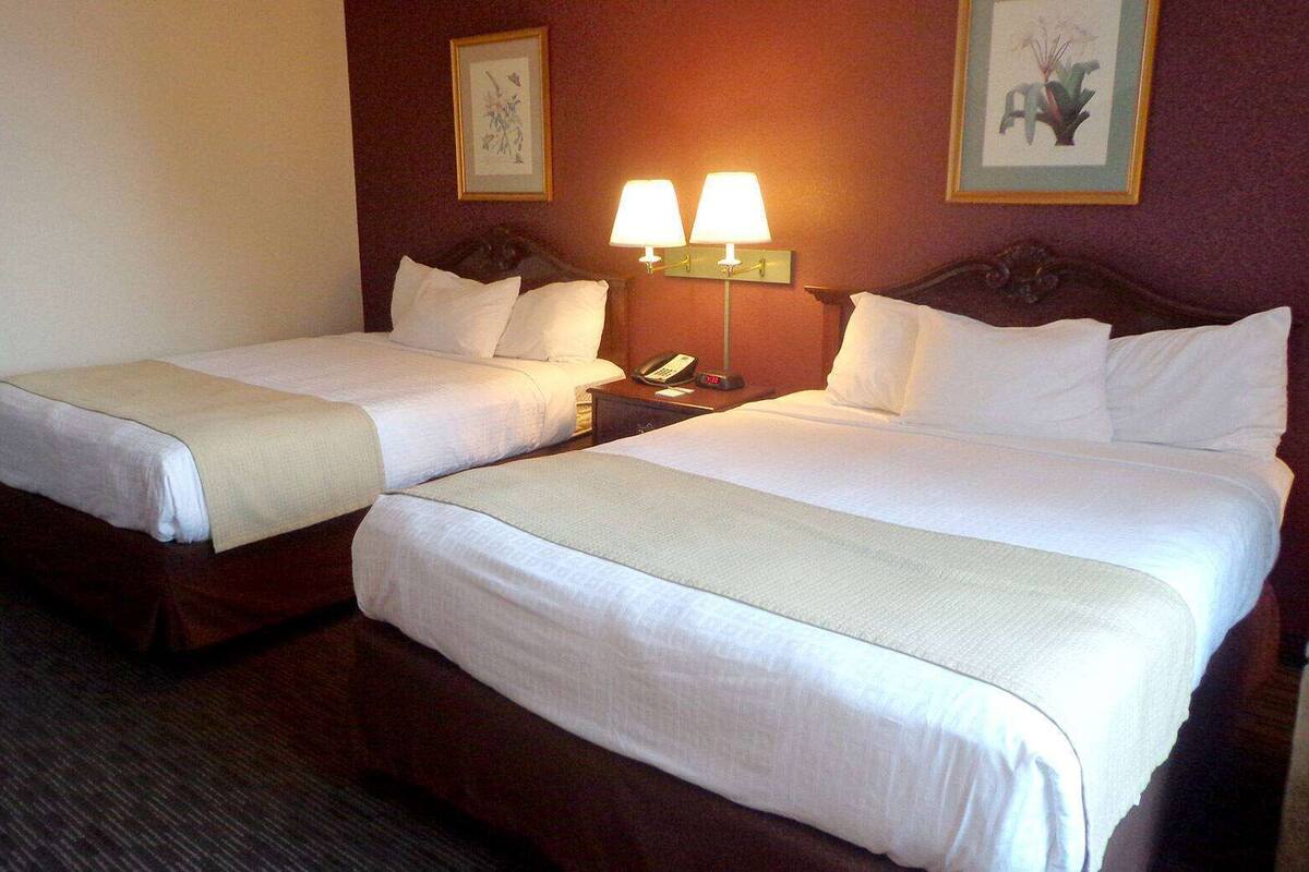 A hotel room with two beds, a nightstand with a lamp, and artwork on the walls.