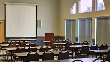 Une salle de conférence équipée de tables, de chaises, d’un écran de projection et de grandes fenêtres.