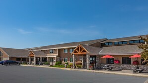 A hotel with a covered outdoor seating area, a parking lot, and a clear blue sky. - AmericInn by Wyndham Marshall (Marshall)