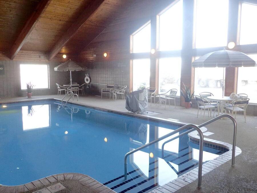 An indoor swimming pool with clear water, surrounded by a tiled area with chairs and tables.