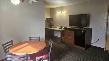 Habitación pequeña con una mesa redonda de madera y sillas, una kitchenette con microondas, cafetera y un televisor en un mueble.