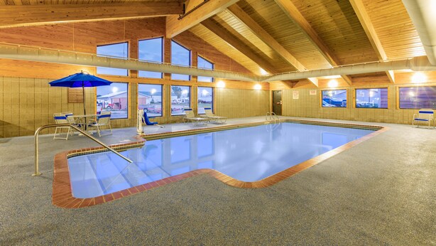 An indoor swimming pool with a wooden ceiling, large windows, and a blue umbrella. - AmericInn by Wyndham Marshall (Marshall)