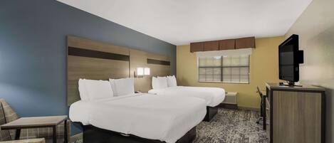 A hotel room with a large bed, a desk, a chair, a television, and a window.