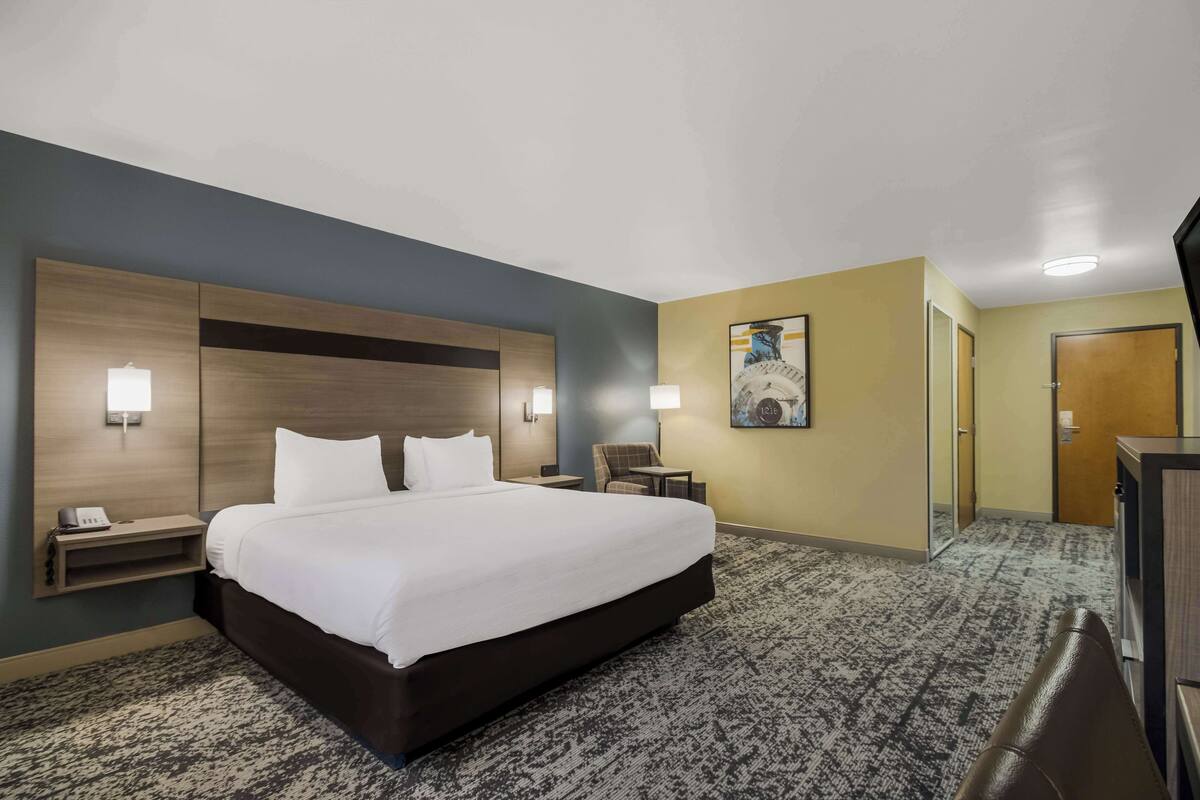 Ein Hotelzimmer mit einem großen Bett, Nachttischen, einem Schreibtisch, einem Sessel und einem Bild an der Wand.