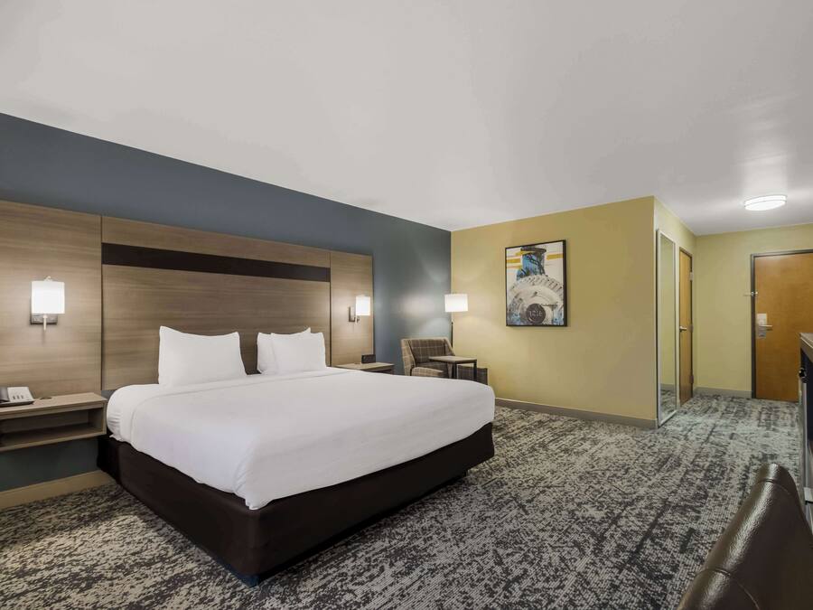 A hotel room with a large bed, bedside tables, a desk, a chair, and a painting on the wall.