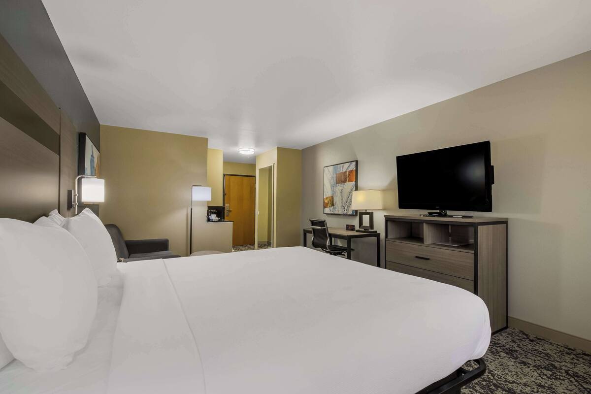 Ein Hotelzimmer mit einem großen Bett, einem Schreibtisch mit Stuhl, einem Fernseher und einer Lampe.
