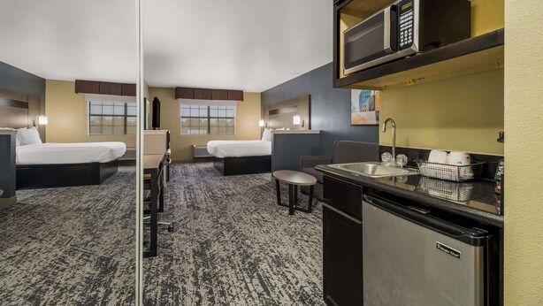 A hotel room with two beds, a small kitchenette, a microwave, a sink, and a window.