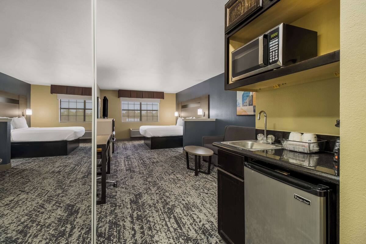 Ein Hotelzimmer mit zwei Betten, einer kleinen Küchenzeile, einer Mikrowelle, einem Spülbecken und einem Fenster.