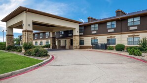 A multi-story hotel with a covered entrance, stone pillars, and a parking lot.