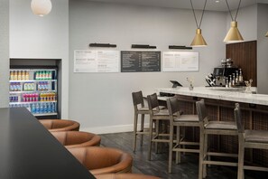 Un espace bar moderne doté d’un tableau affichant le menu, de sièges et d’un distributeur de boissons.