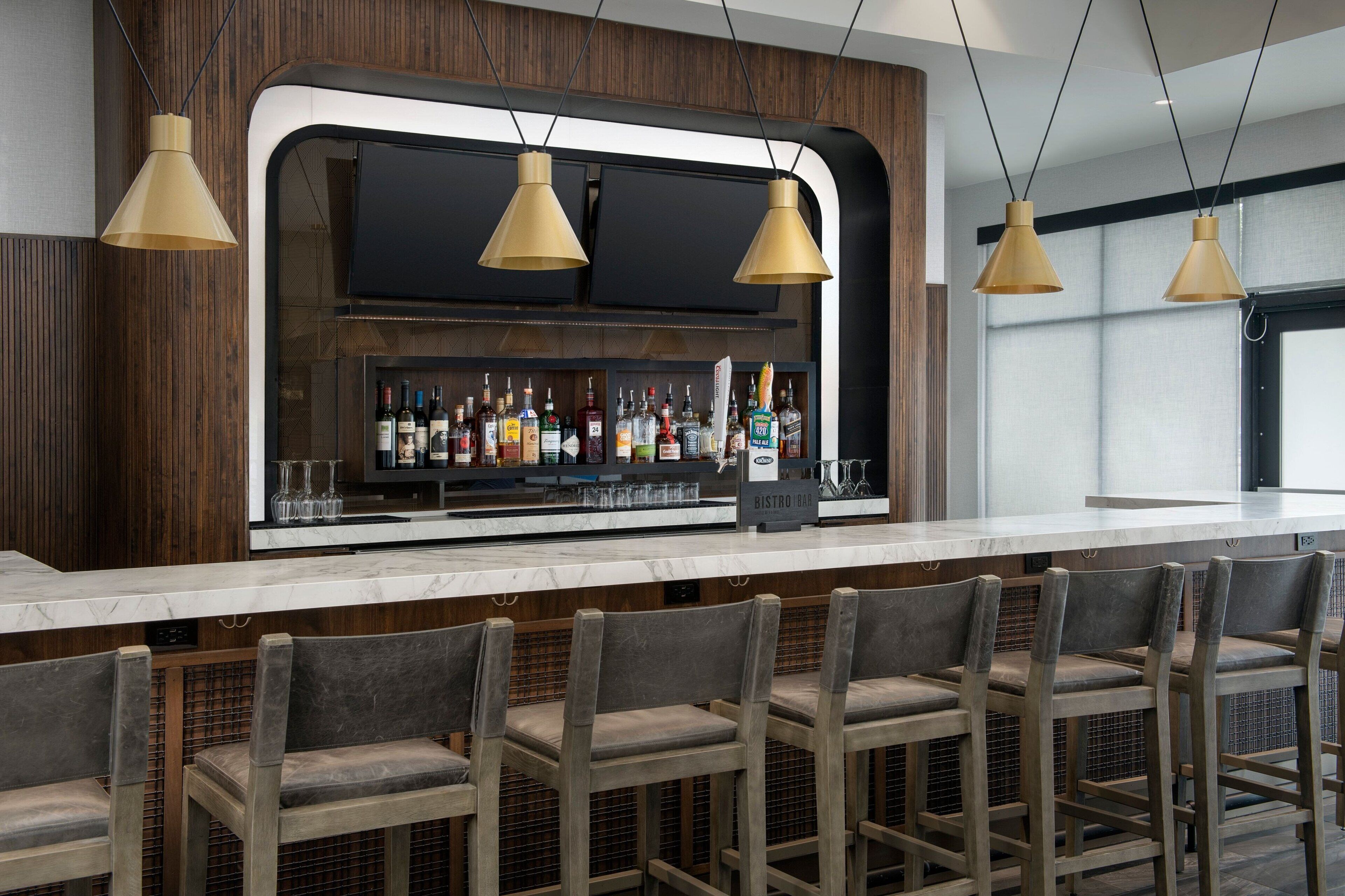 Un espace bar doté d’un comptoir en marbre, de tabourets de bar en bois et d’une variété de bouteilles et de verres.