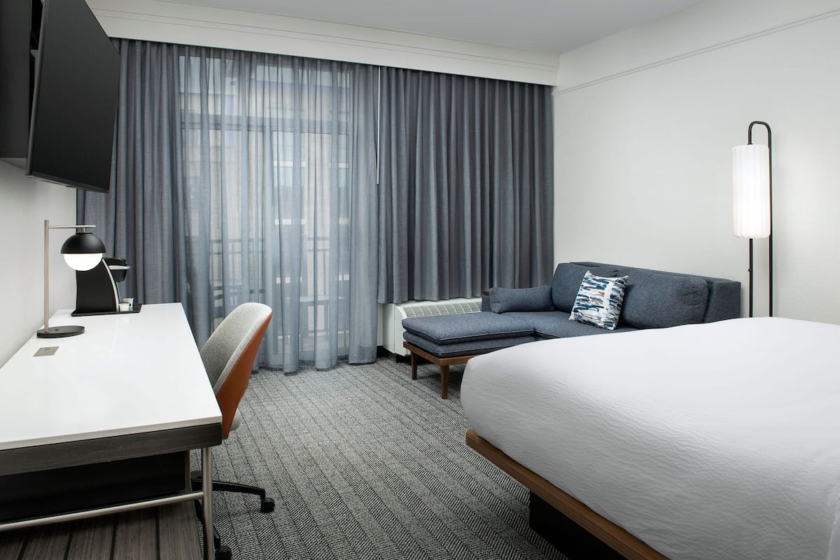 A hotel room with a bed, a desk, a chair, a sofa, and a TV.