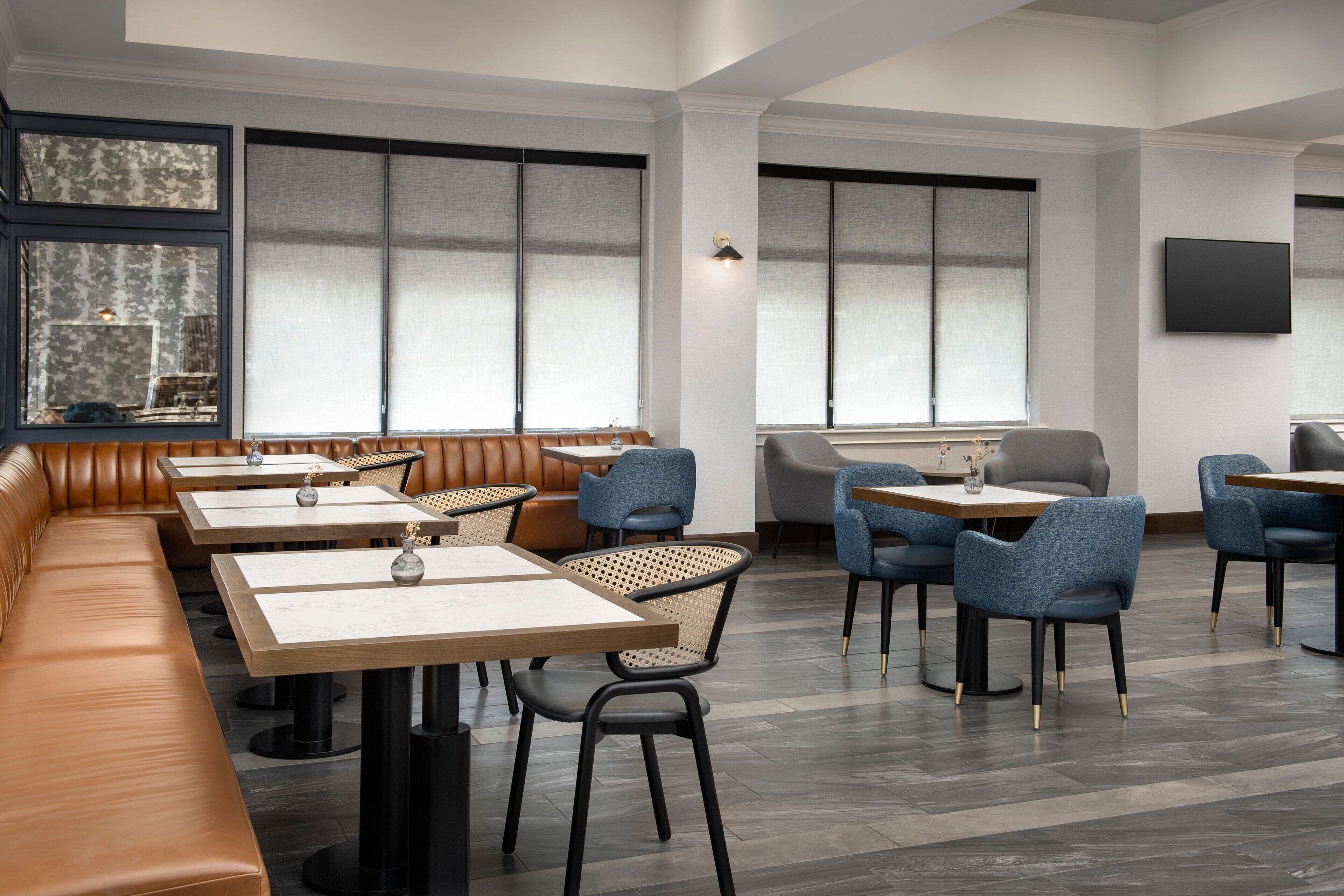 Un interior de restaurante moderno con techos altos, ventanas amplias y diversas opciones de asientos, incluyendo cabinas y mesas.
