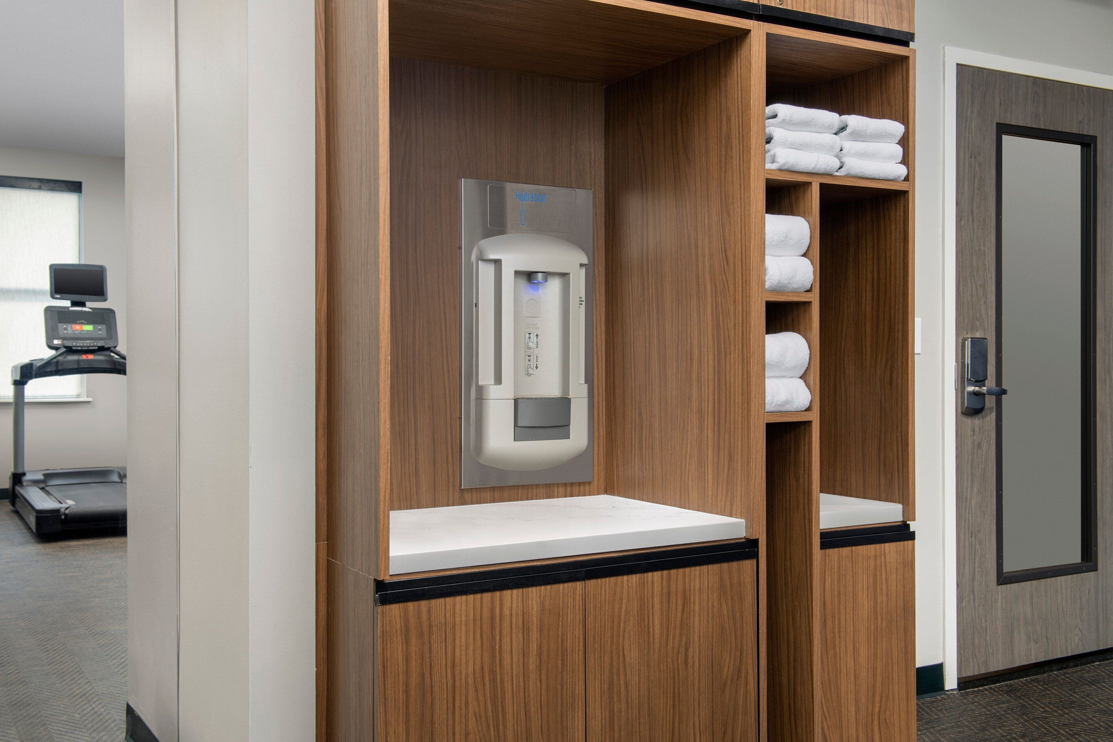 Un bagno d'albergo con erogatore di asciugamani, pesa persona e asciugamani piegati ordinatamente sugli scaffali.