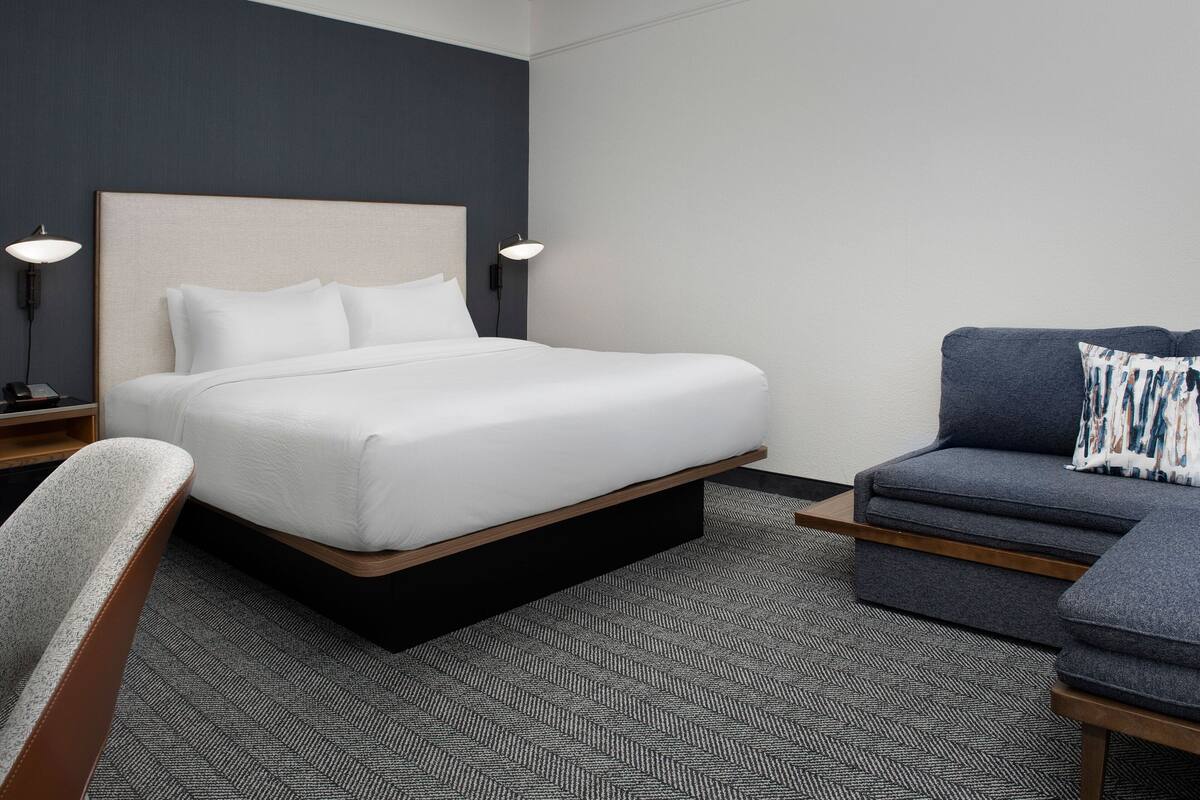 A hotel room with a bed, a sofa, a chair, and two bedside lamps.