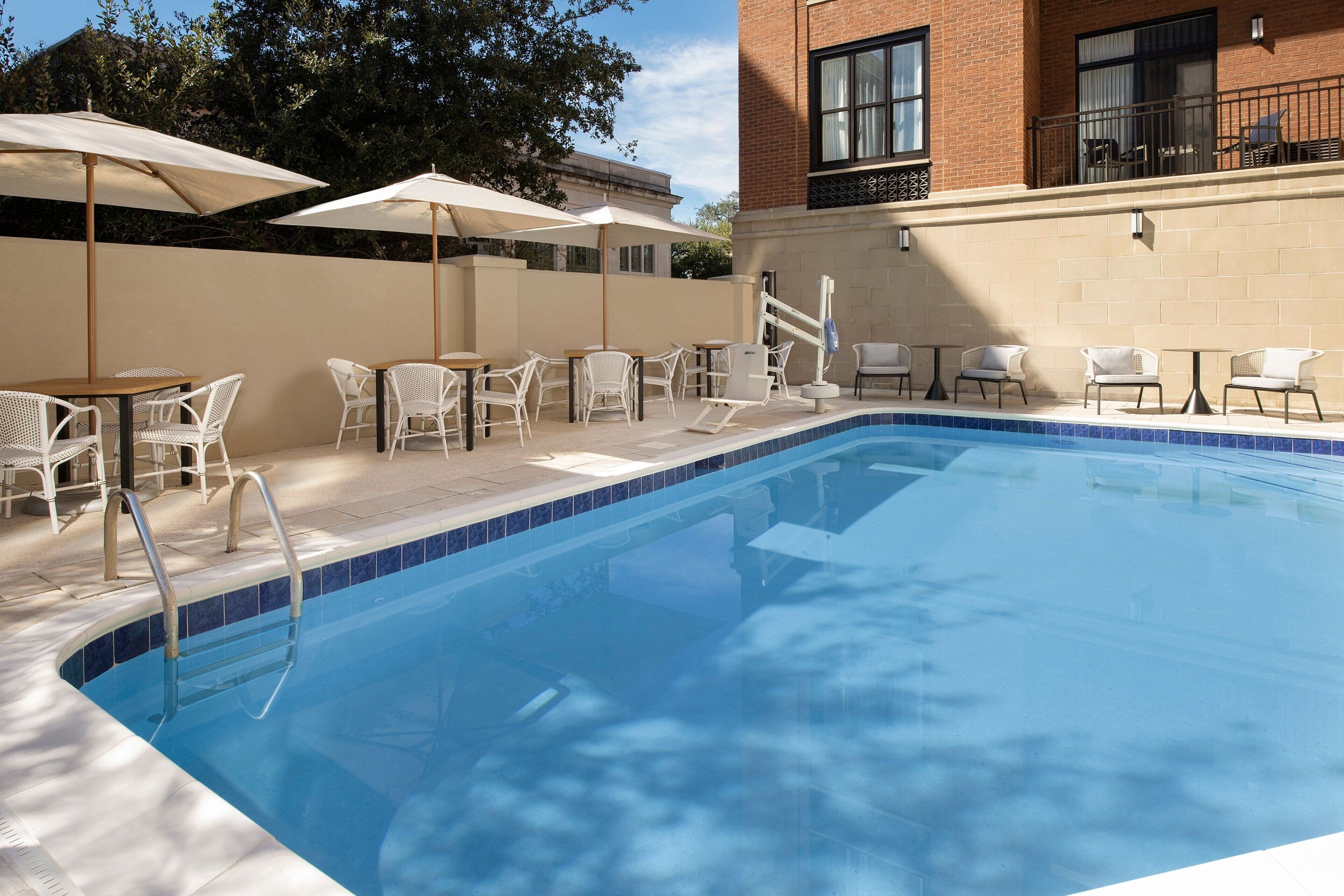Una piscina con sillas de mimbre blanco y sombrillas, rodeada por un edificio de ladrillo.