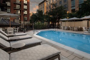 Une piscine entourée d’une clôture et d’arbres, avec des chaises longues et des parasols.