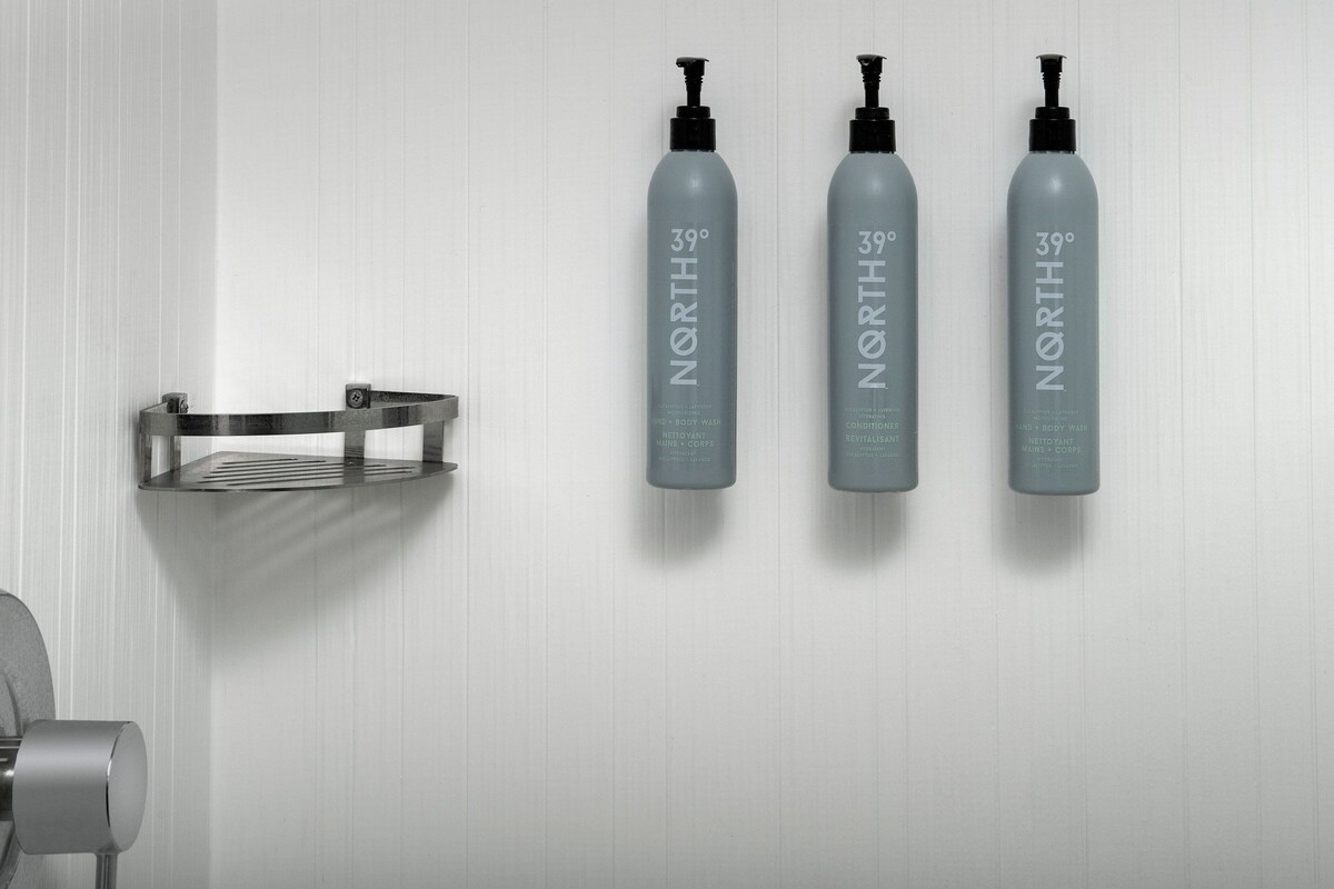 Trois bouteilles de gel douche et d’après-shampoing North 39°, posées sur un mur blanc.