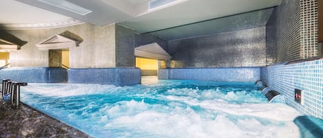 Una piscina interior ampla amb aigua cristal·lina, parets de rajola i terra de pedra.
