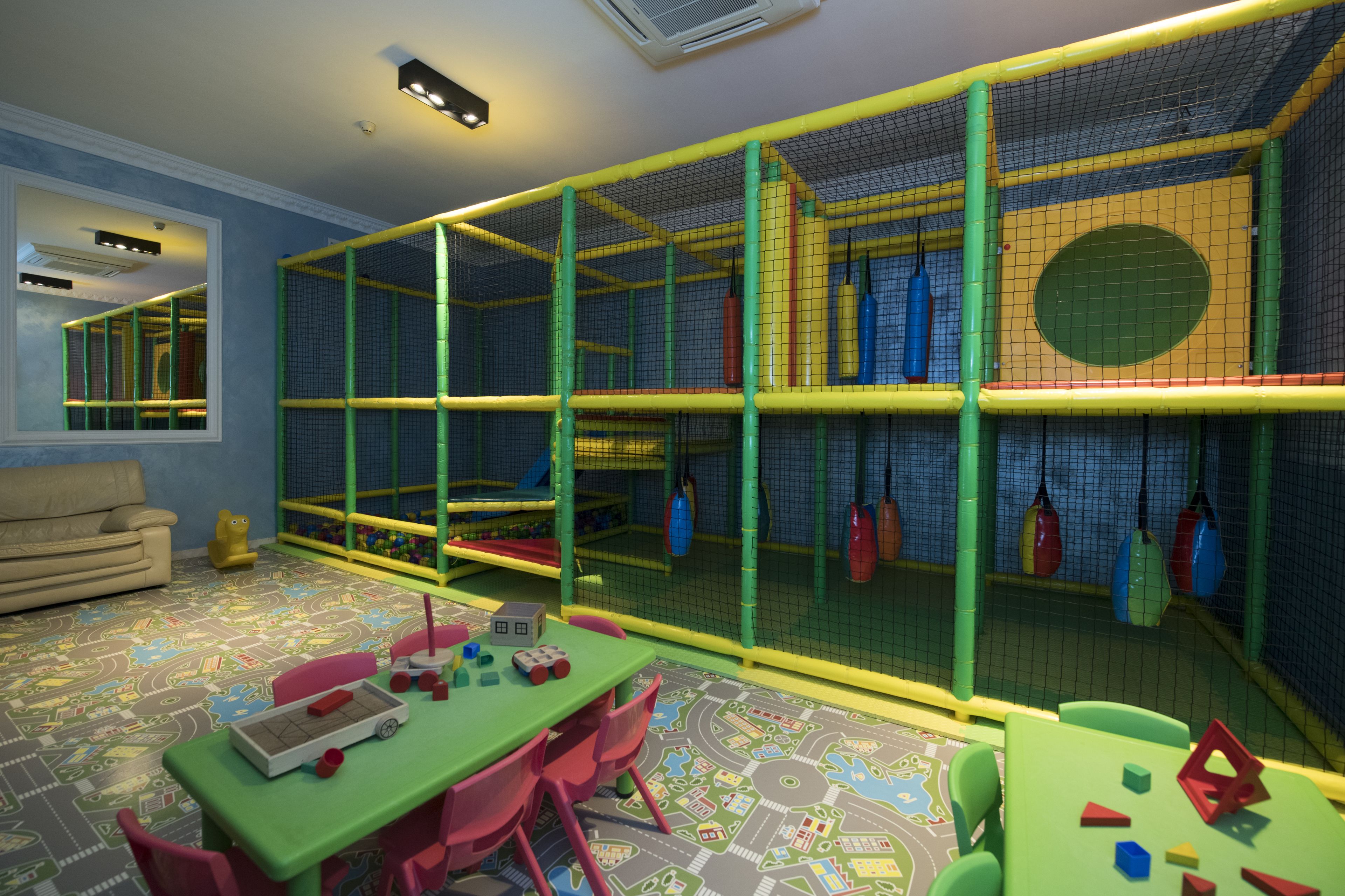 A playroom with a green table, pink chairs, and a playpen with toys.