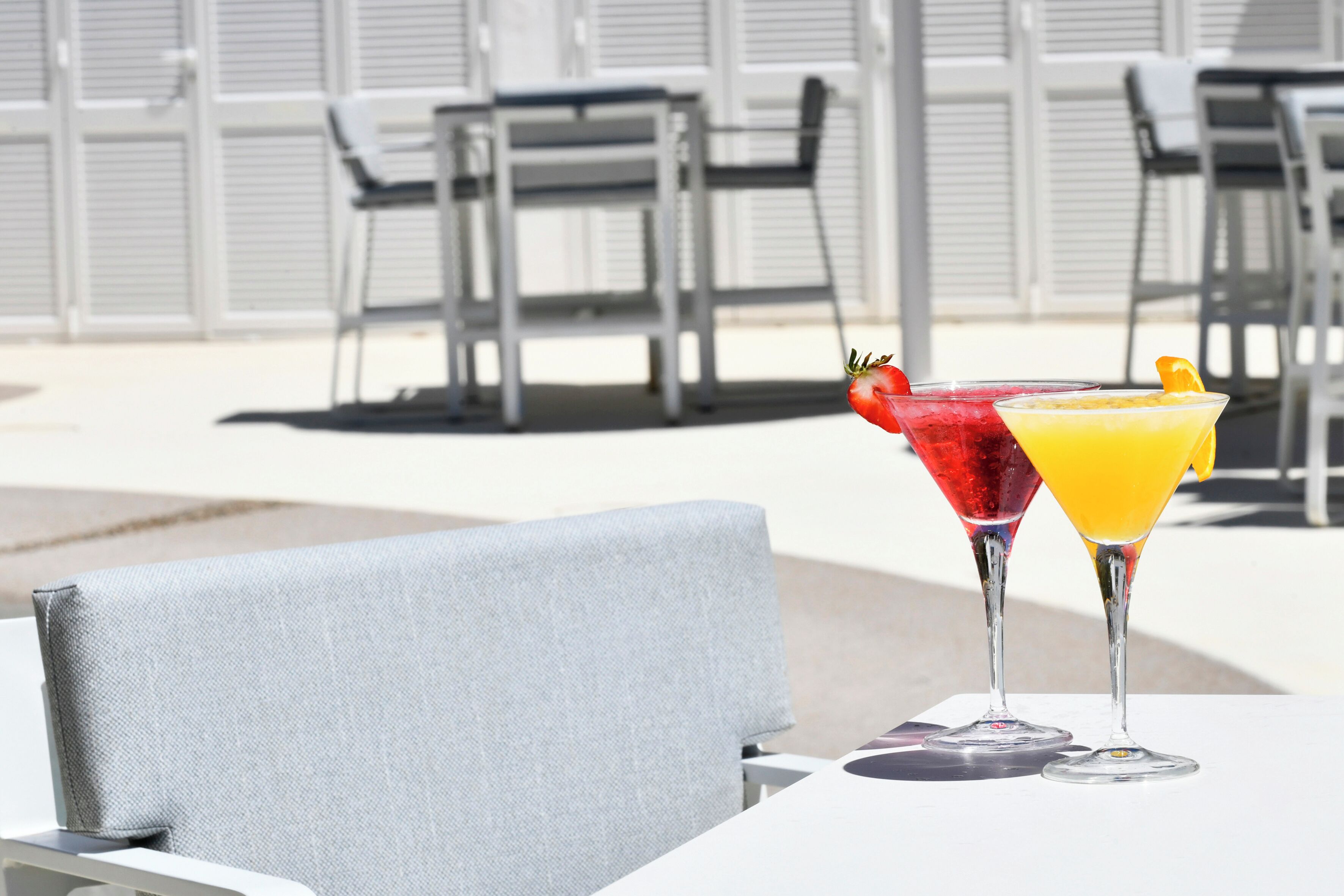 A table with two martini glasses containing cocktails, a grey upholstered chair, and a white tablecloth.
