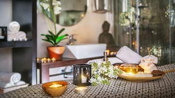 A spa-like setting with a bathtub, candles, flowers, and toiletries on a patterned table.