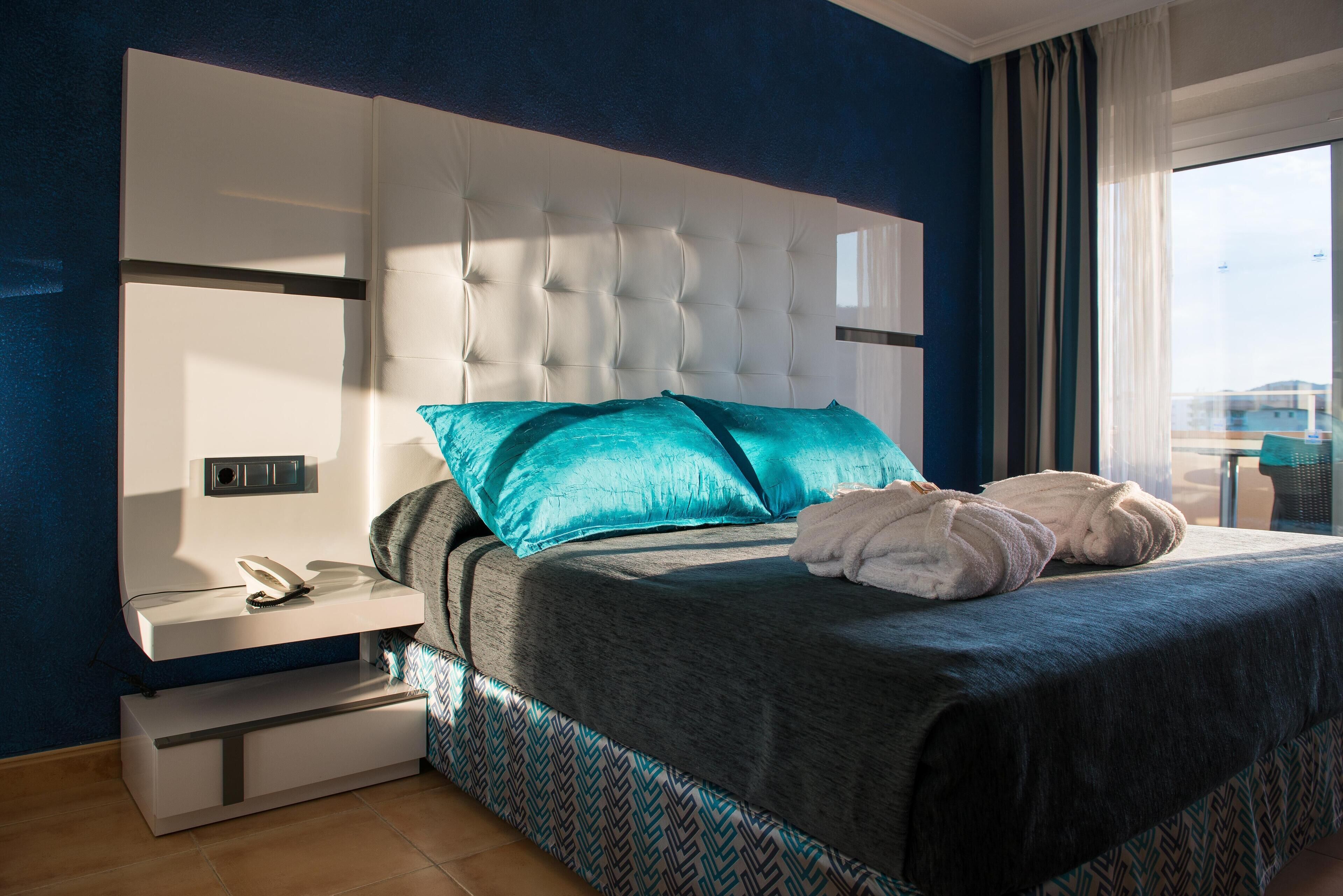 A modern hotel room with a large bed, a bedside table with a phone, and a view of the city.