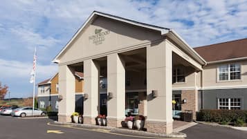 A hotel entrance with a covered porch, a flag, and a parking lot.