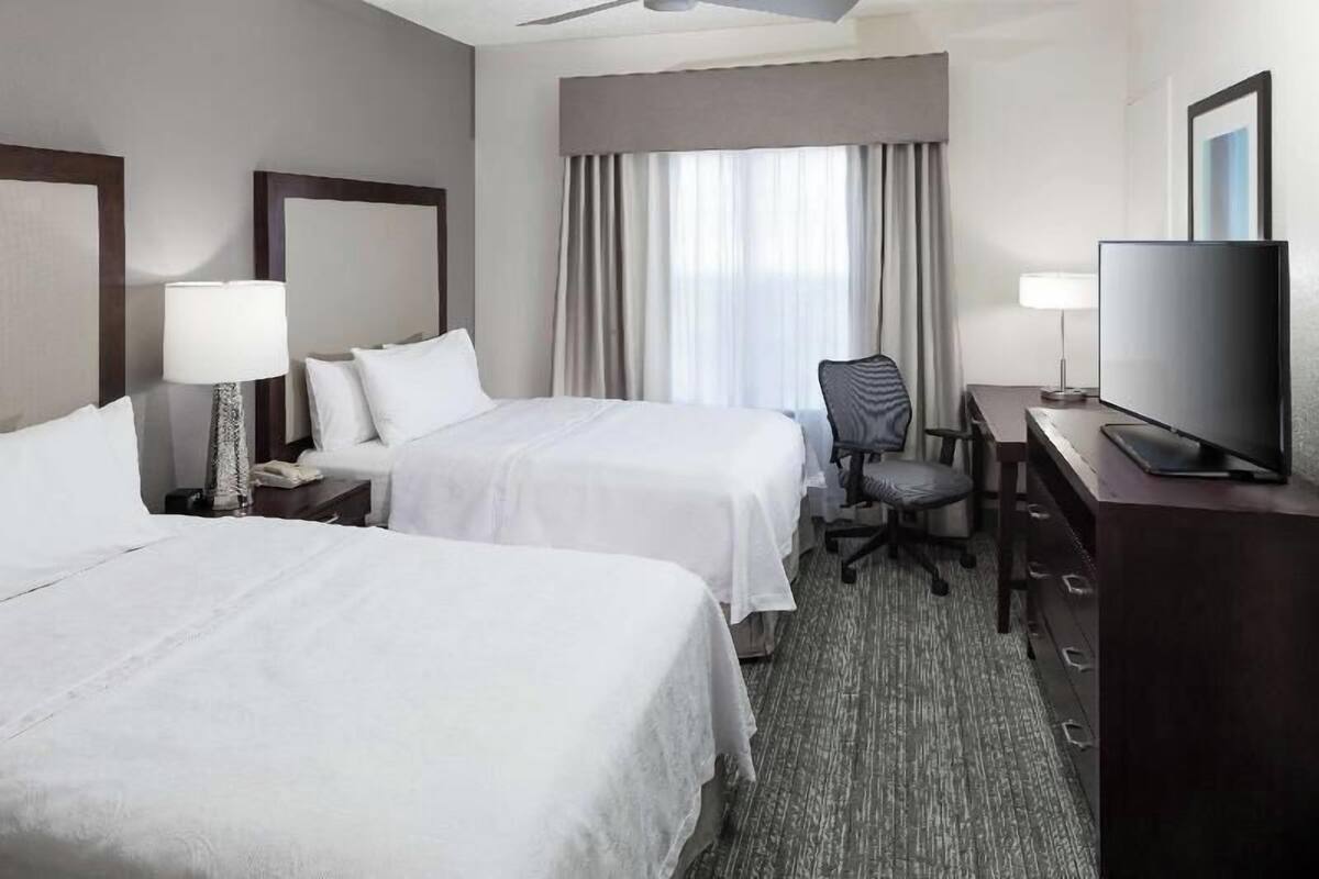 A hotel room with two beds, a desk, a television, and a ceiling fan.