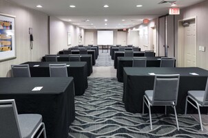 Un salón de conferencias con filas de mesas y sillas, una pantalla de proyector y una señal de salida.