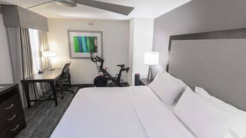Habitación de hotel con una cama grande, un escritorio, una silla, una bicicleta y un ventilador de techo.