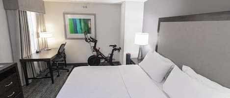 A hotel room with a large bed, a desk, a chair, a bicycle, and a ceiling fan.