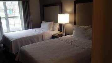 A hotel room with two beds, a bedside lamp, and a window with curtains.