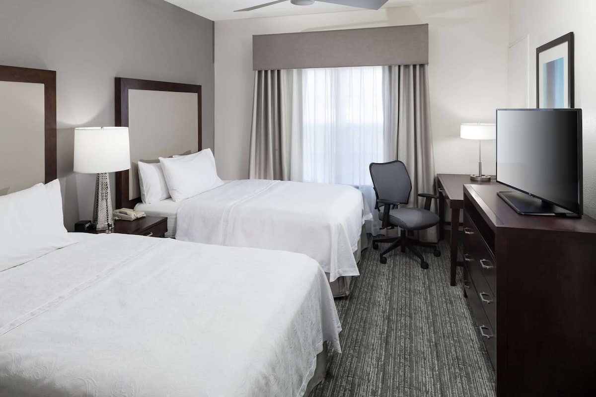 A hotel room with two beds, a desk with a television, a chair, and a desk lamp.