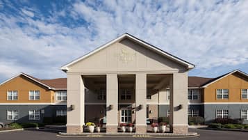 A hotel entrance with a central portico, a sign reading "Homewood Suites Hilton", and a parking area with directional arrows.